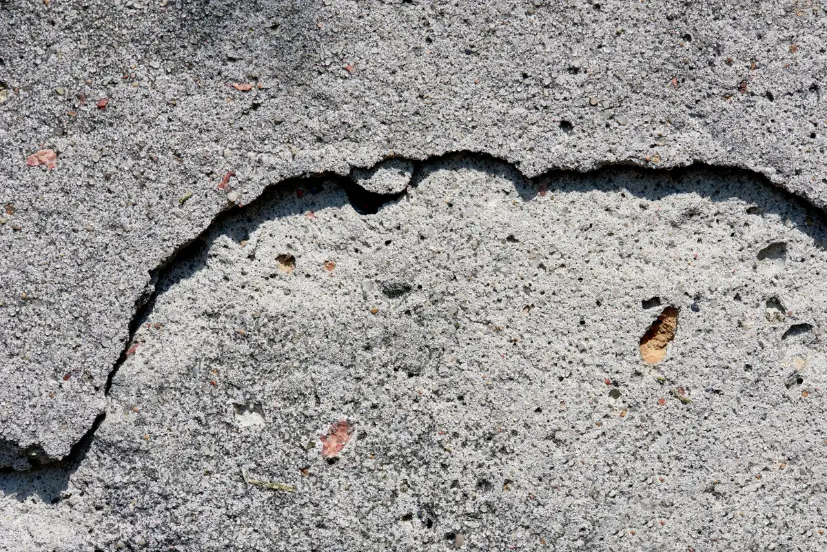 Nahaufnahme rauer Betonoberfläche mit Abplatzungen und Rissen – Betonsanierung
