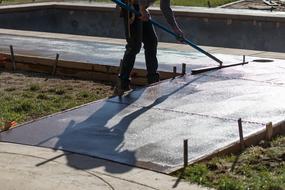 Arbeiter glättet bei Terrassensanierung frisch gegossenen Betonweg neben Pool