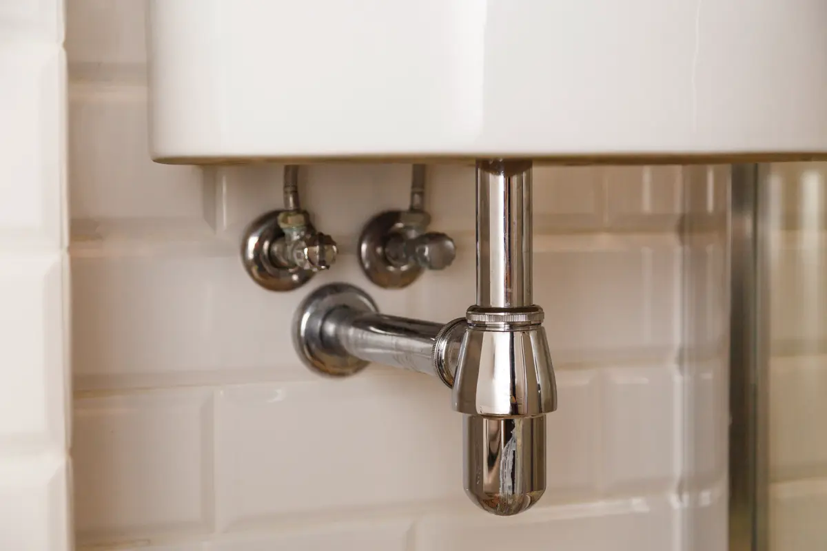 Verchromter Waschbecken-Siphon mit Absperrventilen an Wandfliesen für Rohrreinigung