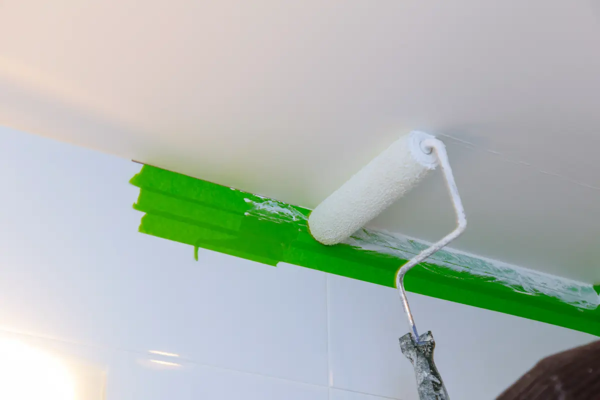 Farbroller mit weißer Farbe gleitet über abgeklemmte Decke mit grünem Klebeband – Malerarbeiten